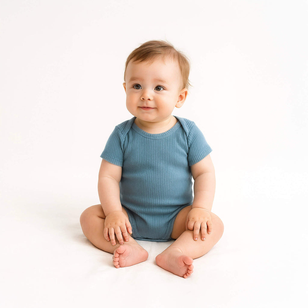 Baby wearing a blue onesie sitting on a white background