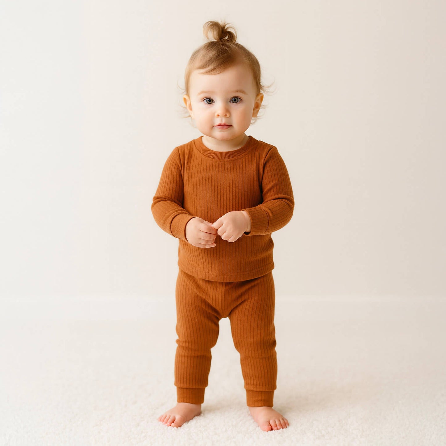 Baby wearing a brown ribbed pajama set in a light background
