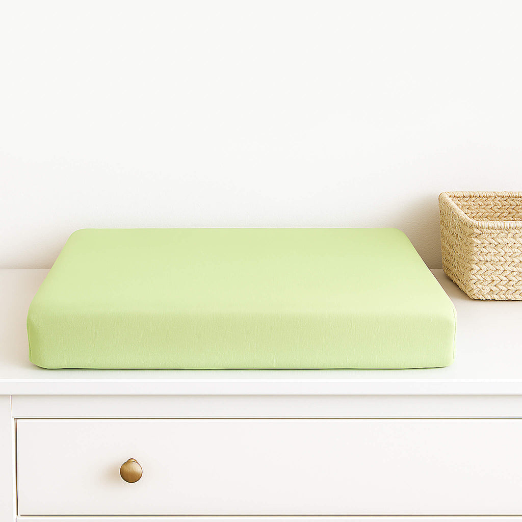 Light green changing pad cover on a white dresser with a woven basket in the background