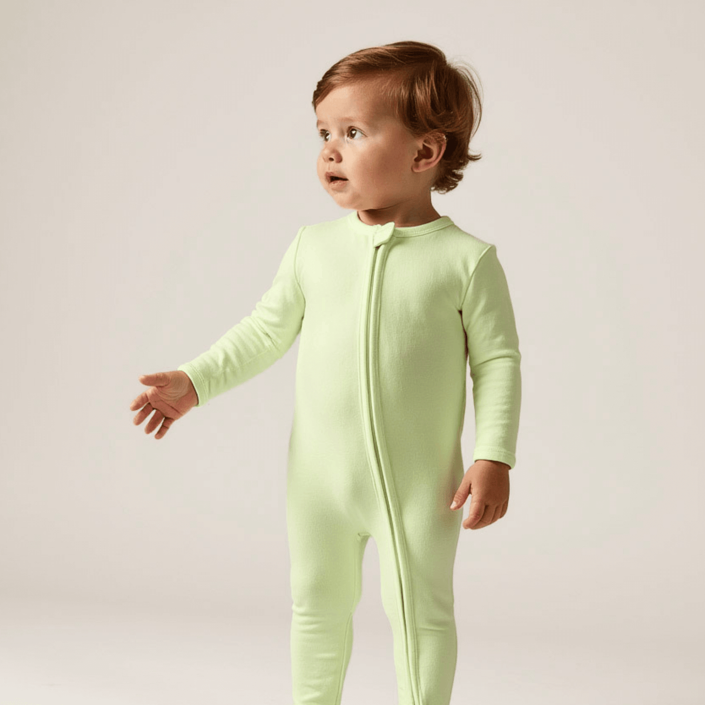 baby standing wearing green footie pajamas