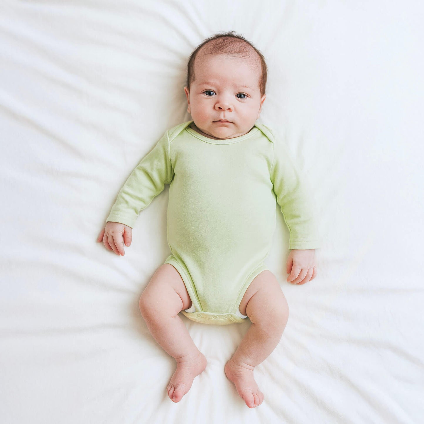 Baby wearing a light green onesie lying on a white surface