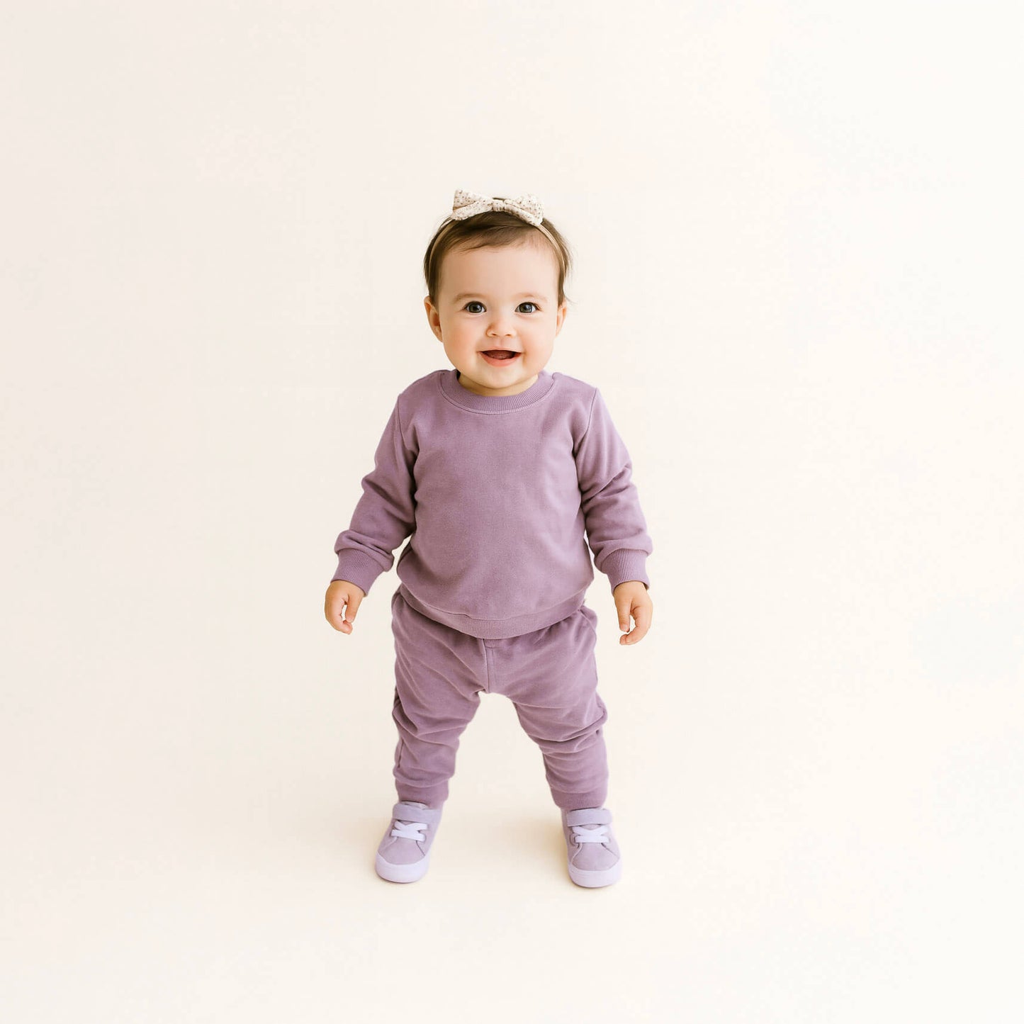 Baby in a purple outfit standing on a light beige background
