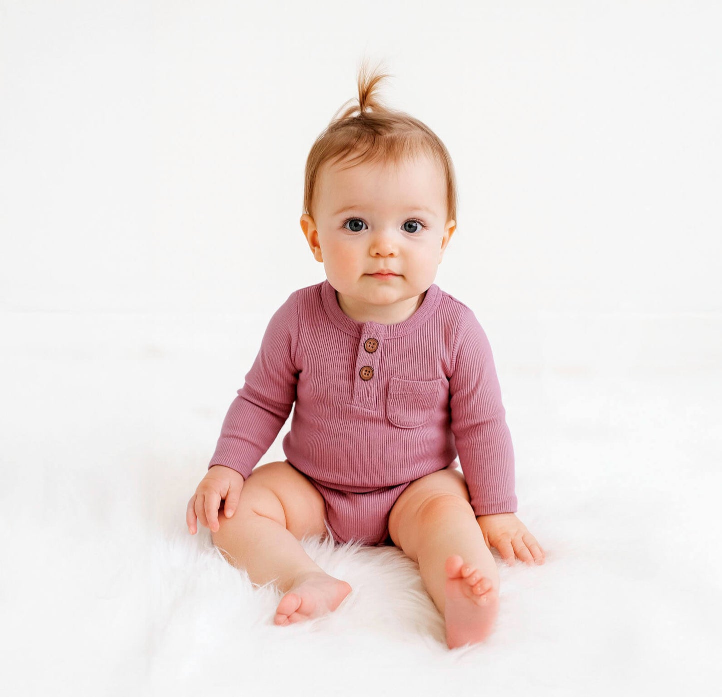 Baby wearing a pink onesie sitting on a white surface