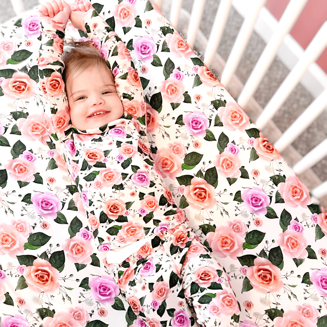 A baby wearing a long-sleeve pajama set with a floral pattern in pink and green colors.
