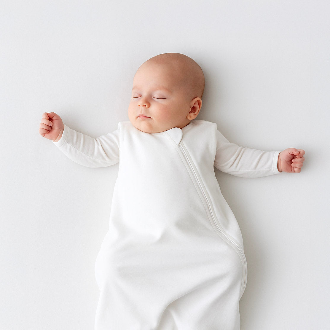 Newborn baby sleeping peacefully in a white sleep sack on a light gray background