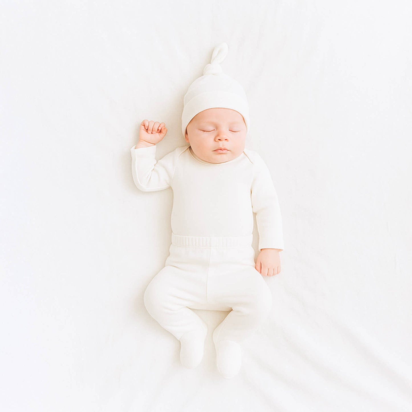 Newborn baby in a white outfit and hat sleeping on a white blanket
