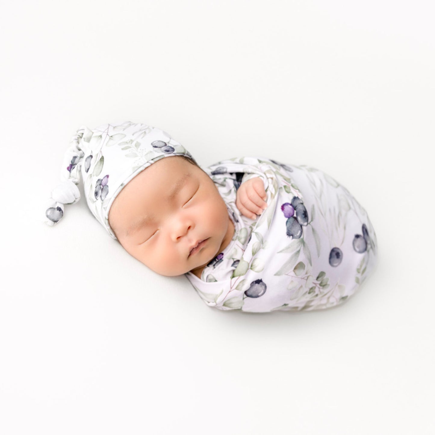 Newborn baby swaddled in a floral blanket with a matching hat on a white background