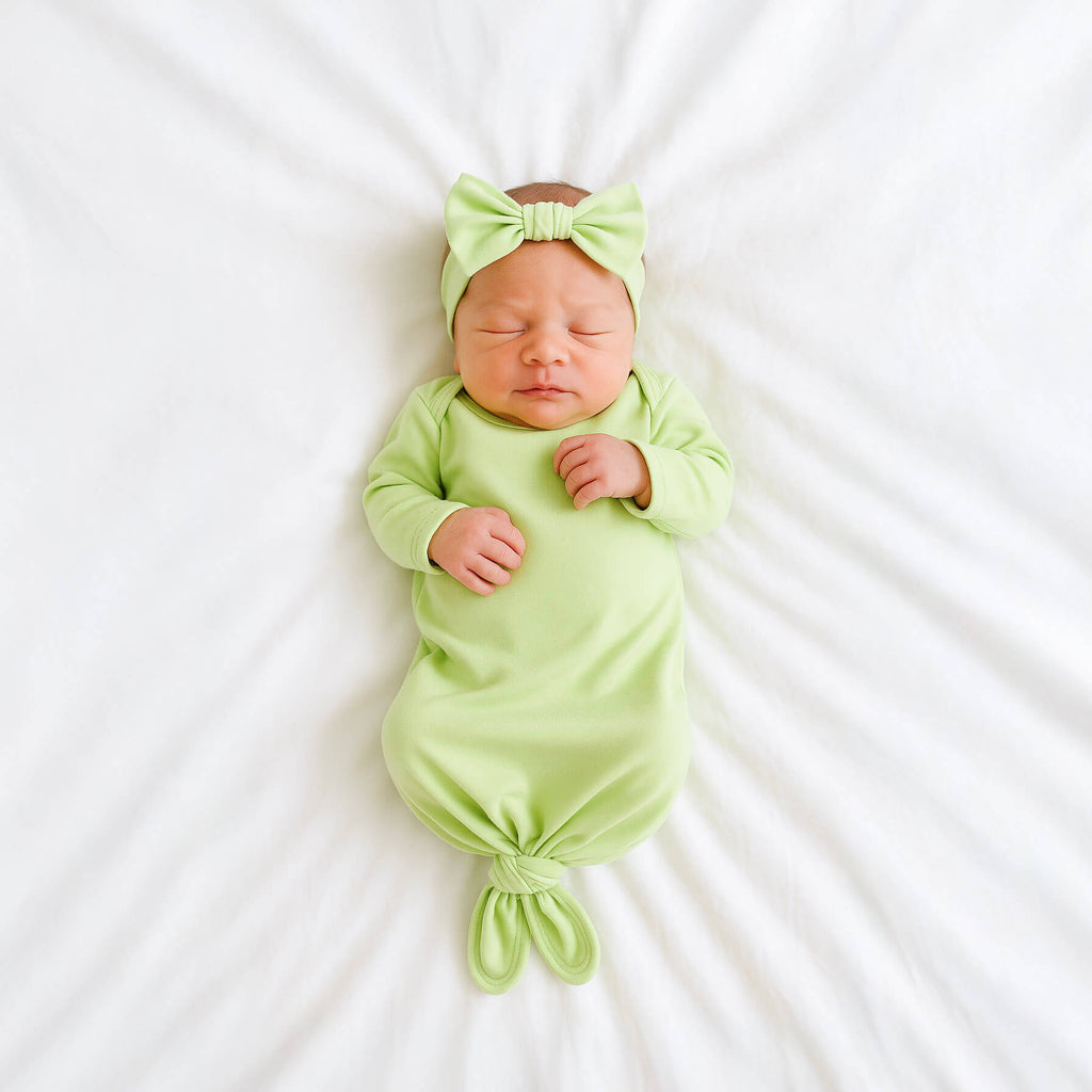 Newborn baby in a green gown set and headband on a white background