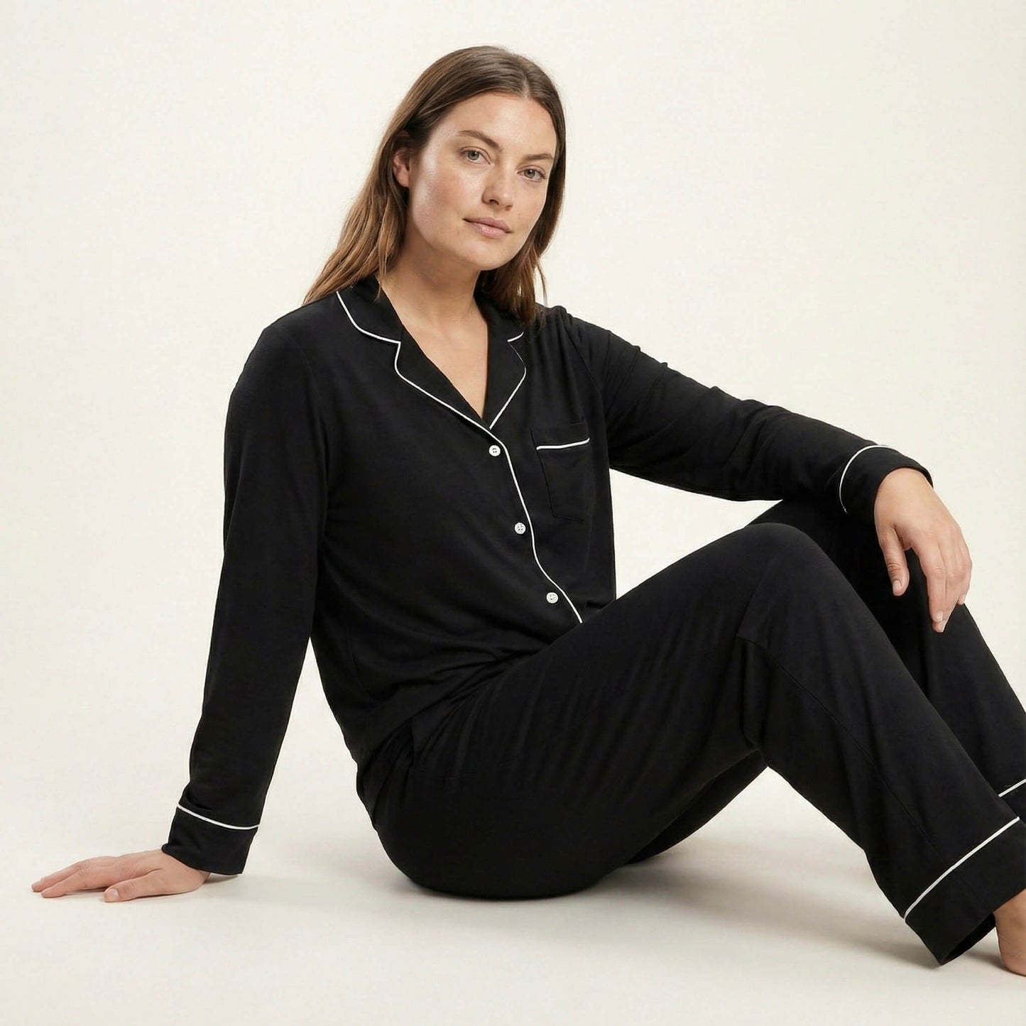 Woman wearing black pajamas with white piping sitting on a white background