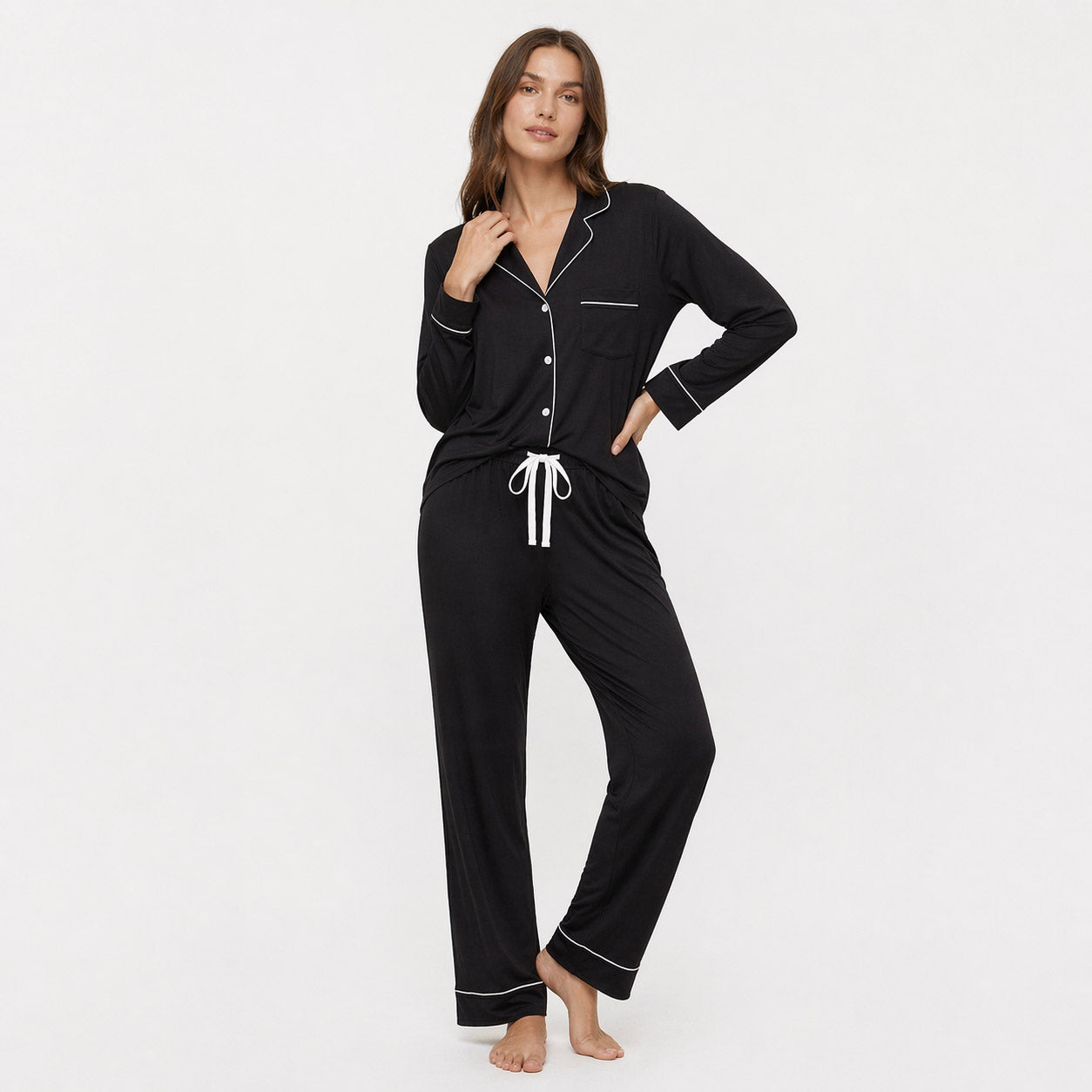 Woman wearing a black pajama set with white piping on a white background