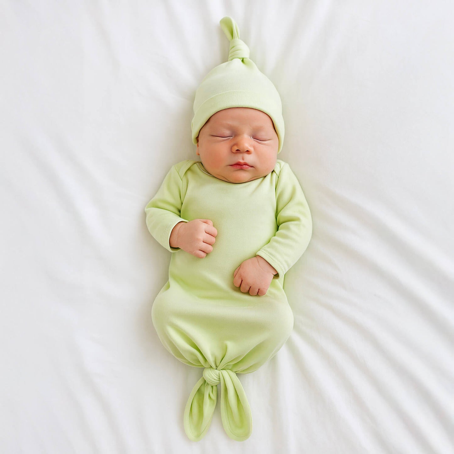 Newborn baby in a light green gown and hat lying on a white surface