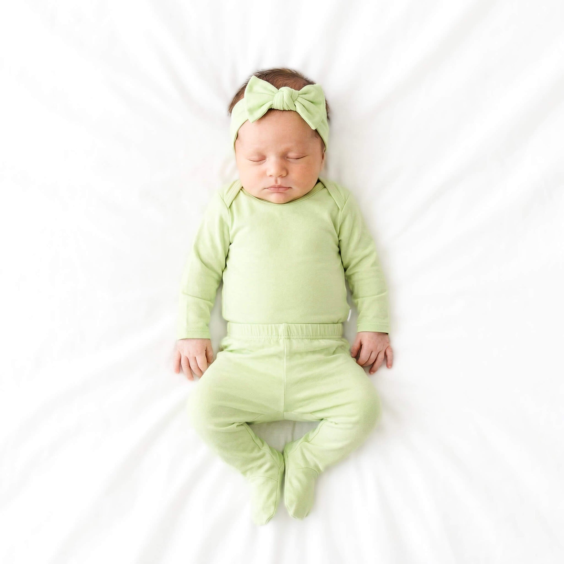 Newborn baby in a green outfit with a matching headband on a white background