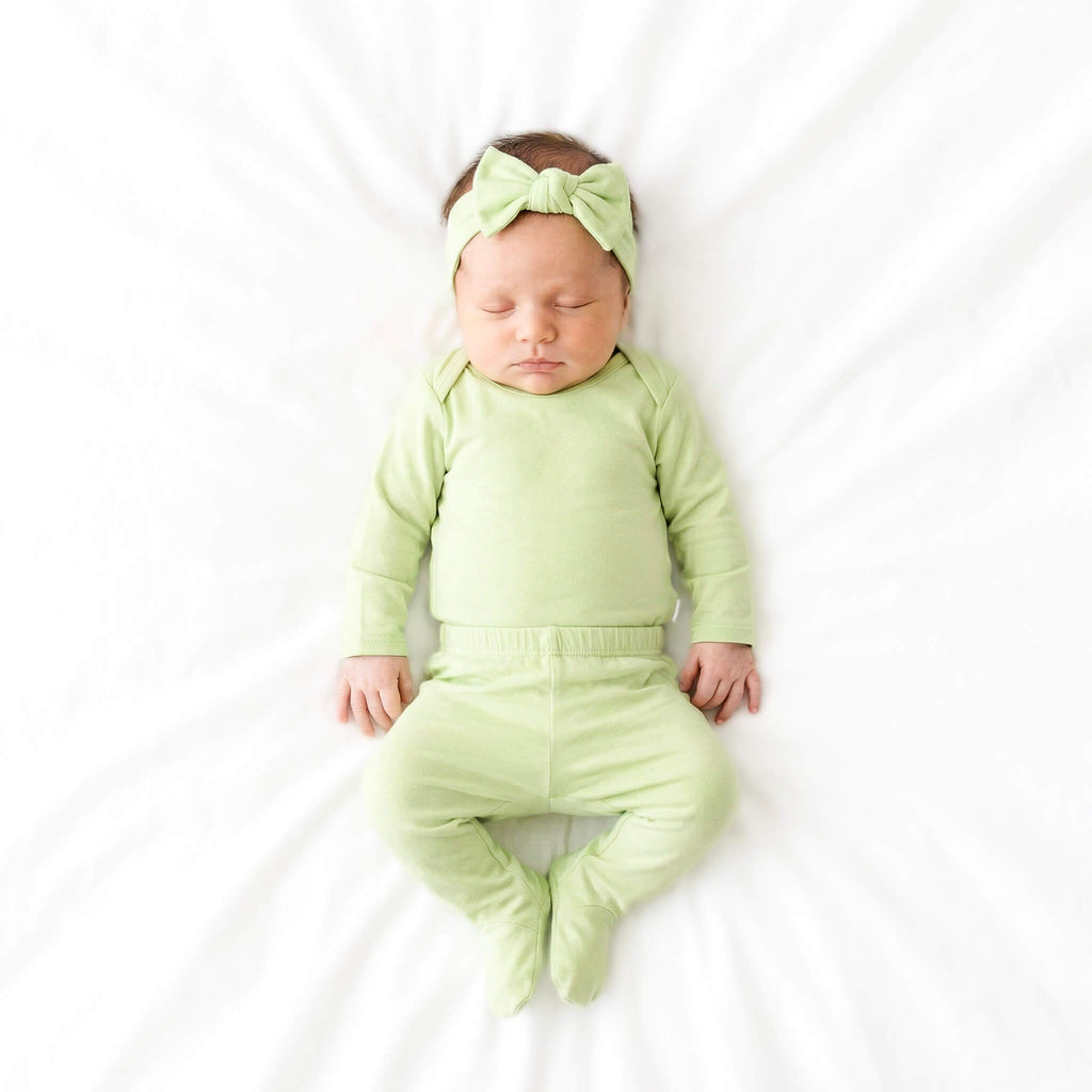 Newborn baby in a green outfit with a matching headband on a white background