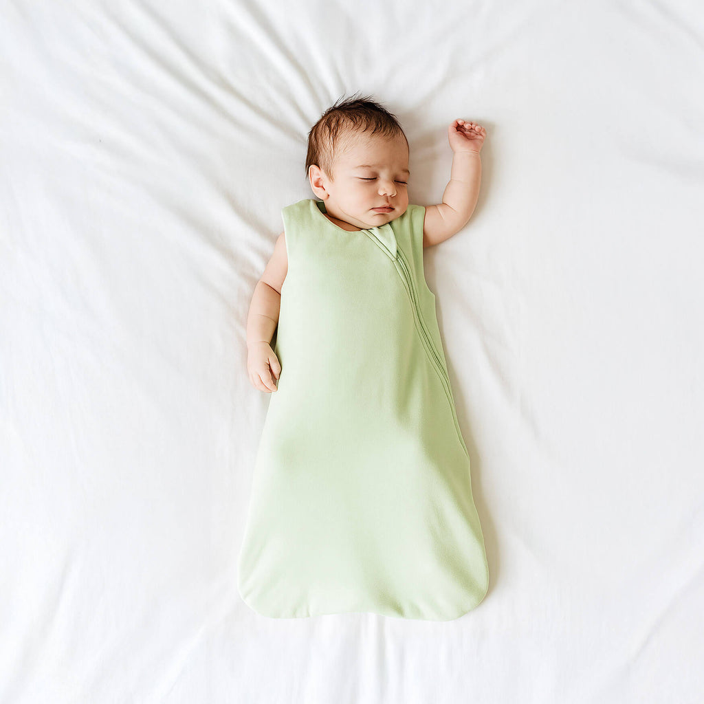 Baby sleeping in a light green sleeveless sleep sack on a white background
