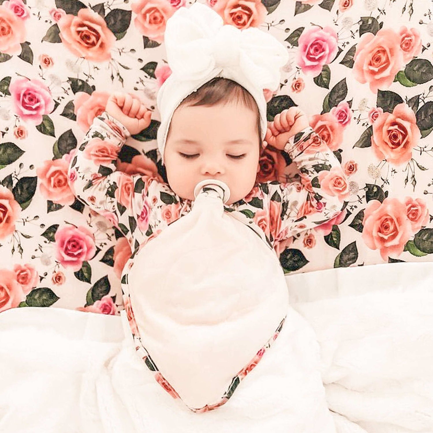 Baby with a pacifier wearing a floral outfit against a floral background