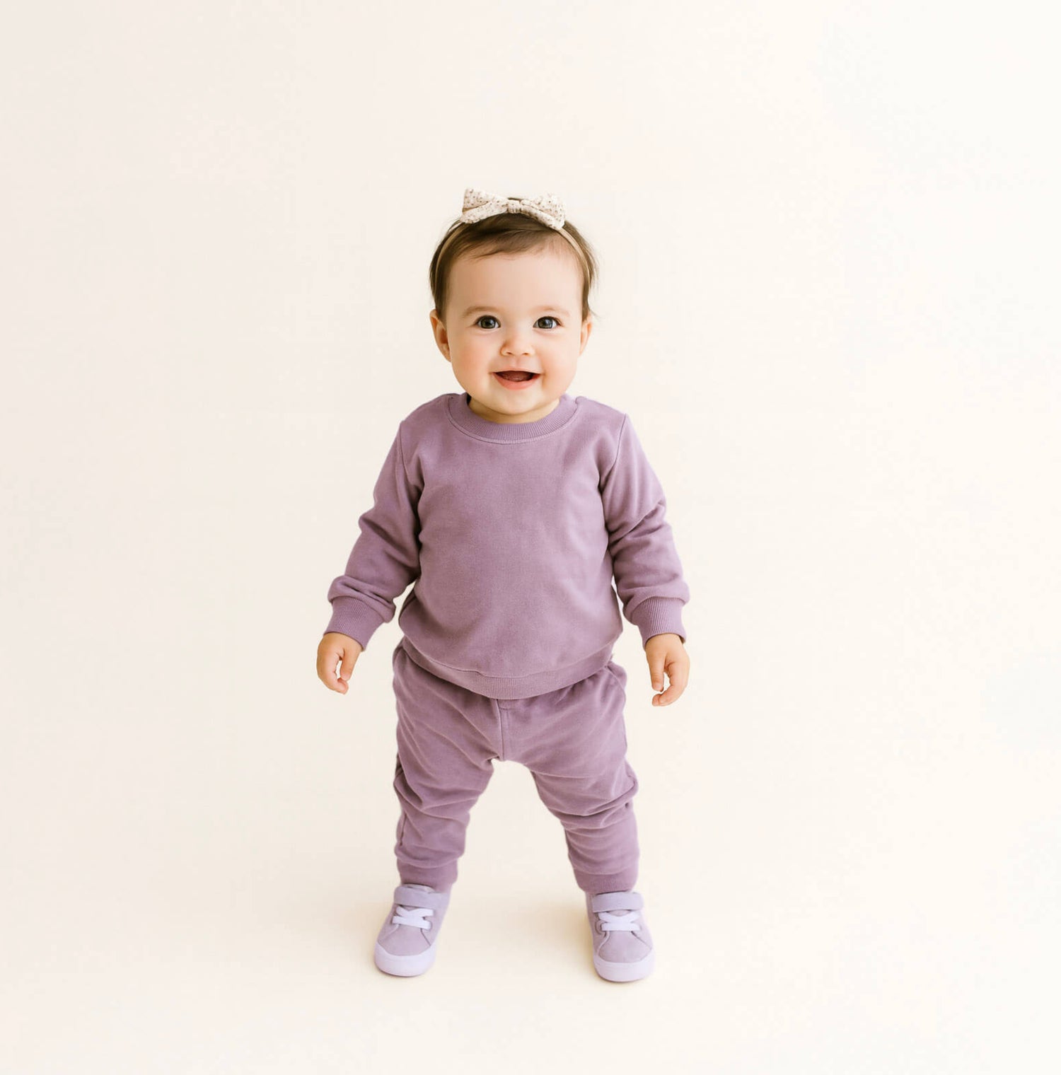 Baby in a purple outfit standing on a light beige background