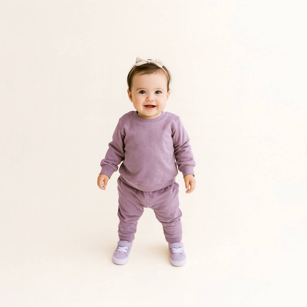 Baby in a purple outfit standing on a light beige background