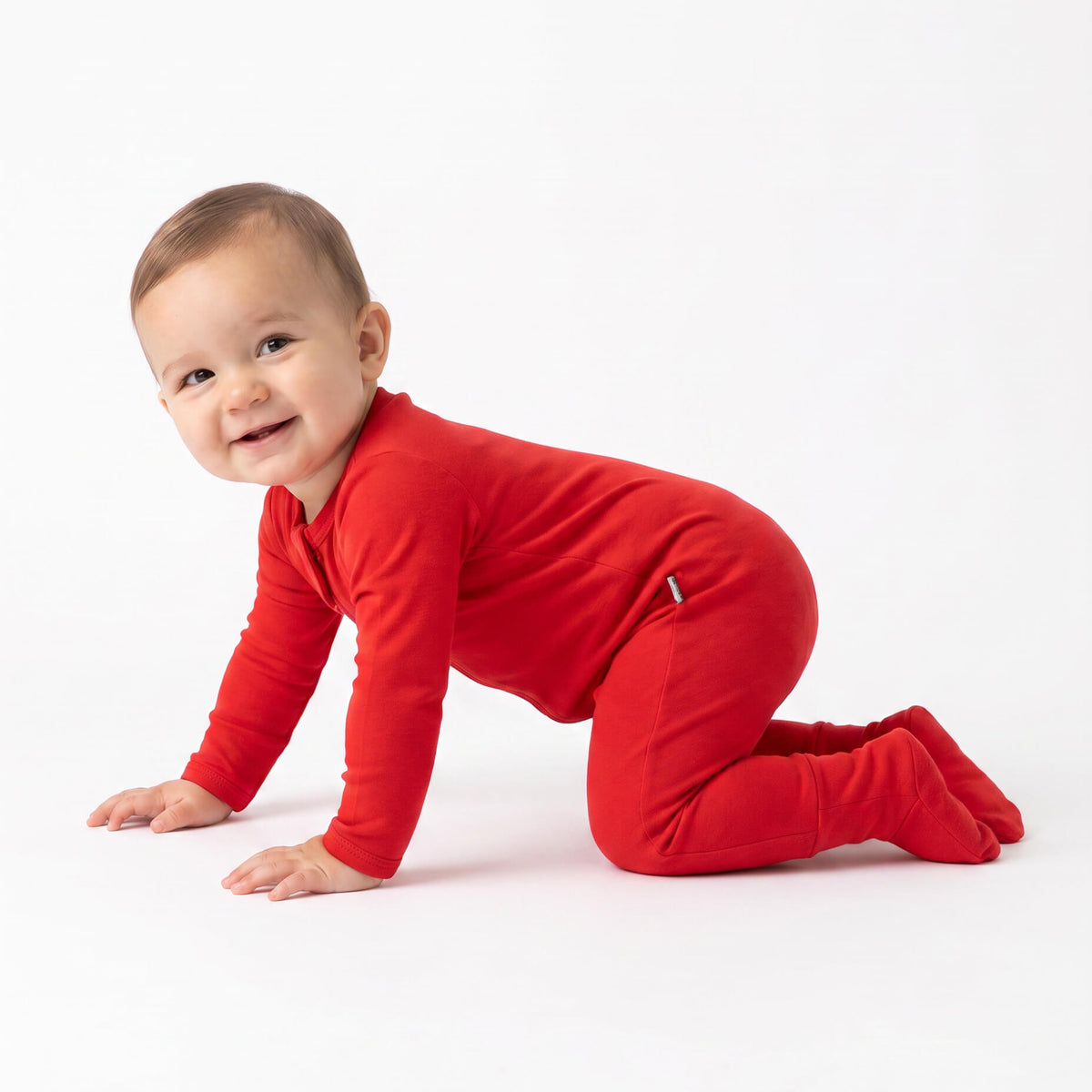 A baby crawling on a white studio floor wearing a bright red long-sleeve footed sleeper.