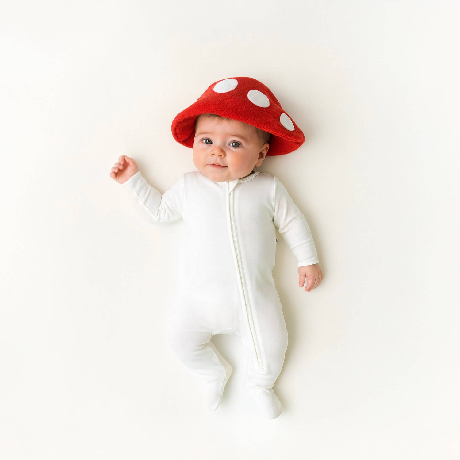 Baby wearing a white onesie and red mushroom hat on a white background
