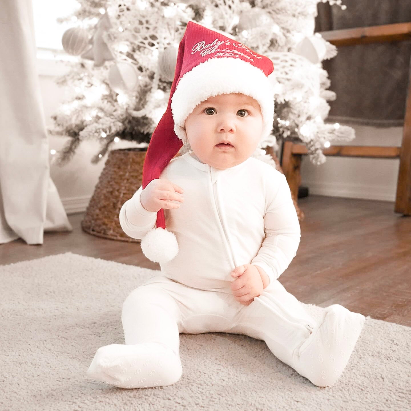 baby wearing white footie pajamas and christmas hat 