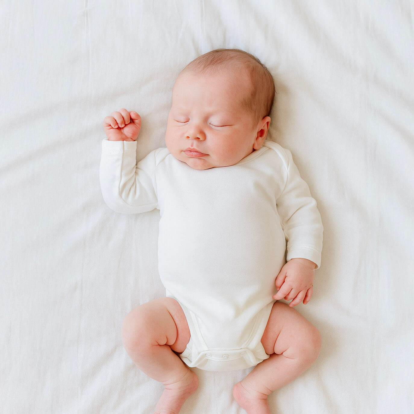Newborn baby in a white onesie lying on a white blanket