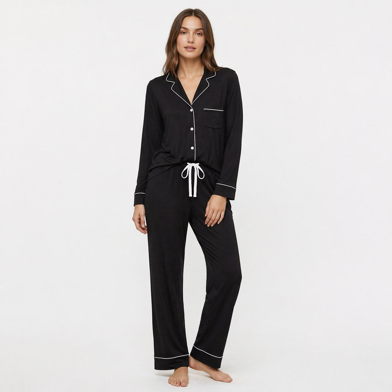 Woman wearing a black pajama set with white piping on a white background