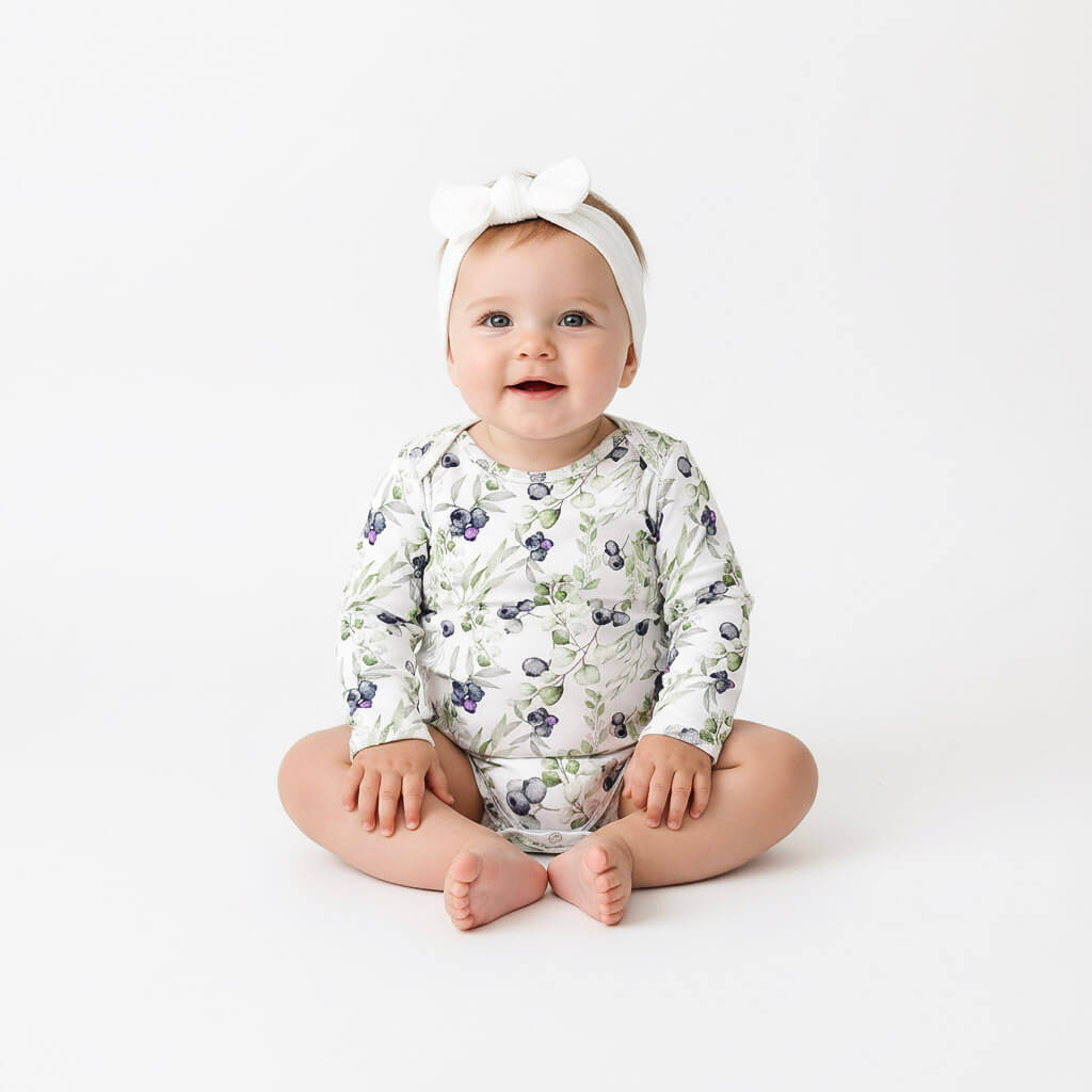 Baby wearing a blueberry onesie and headband on a white background