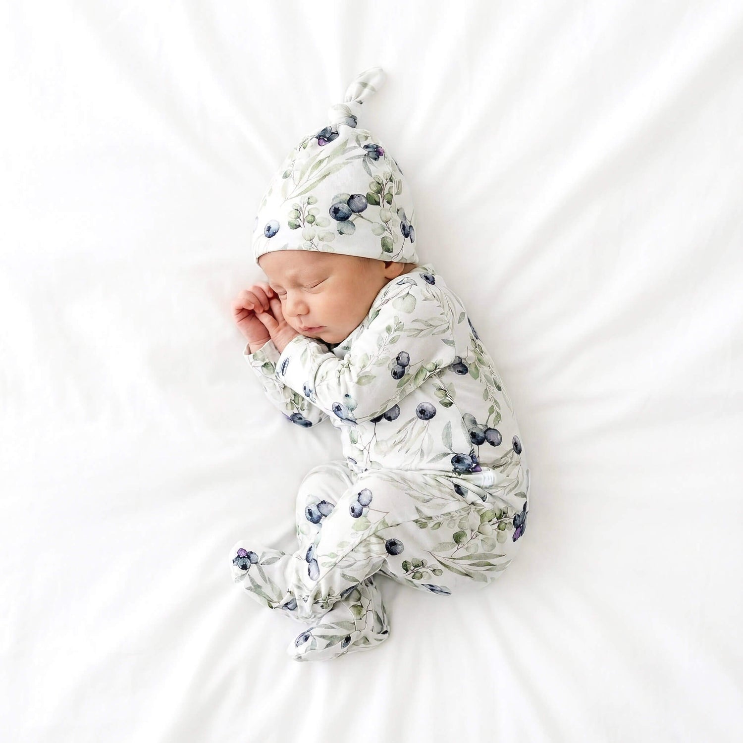 Newborn baby in fa blueberry pattern outfit and hat on a white background