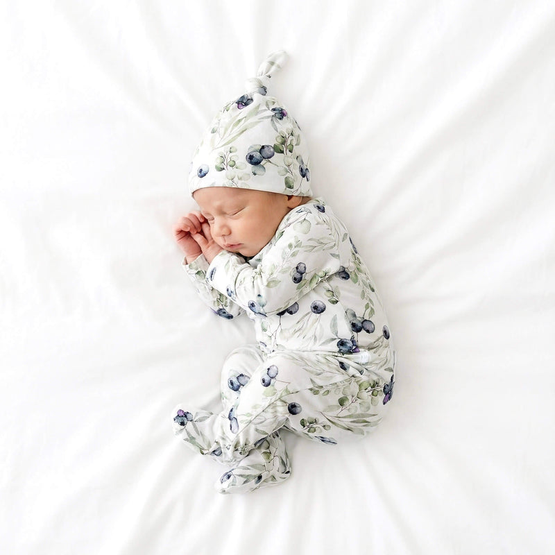 Newborn baby in fa blueberry pattern outfit and hat on a white background