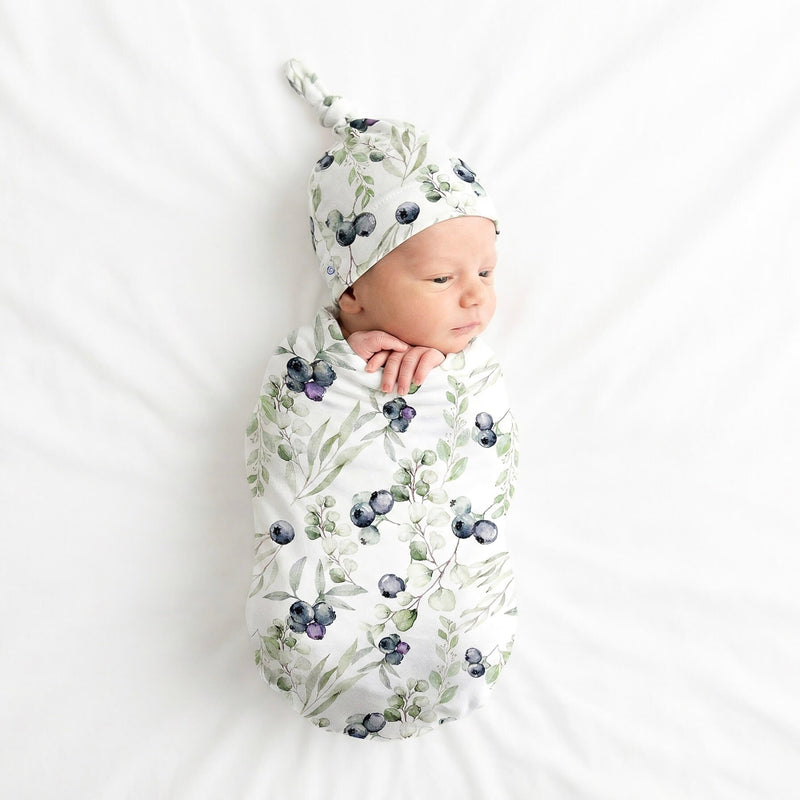 Newborn baby wrapped in a blueberry  swaddle with matching hat on a white background