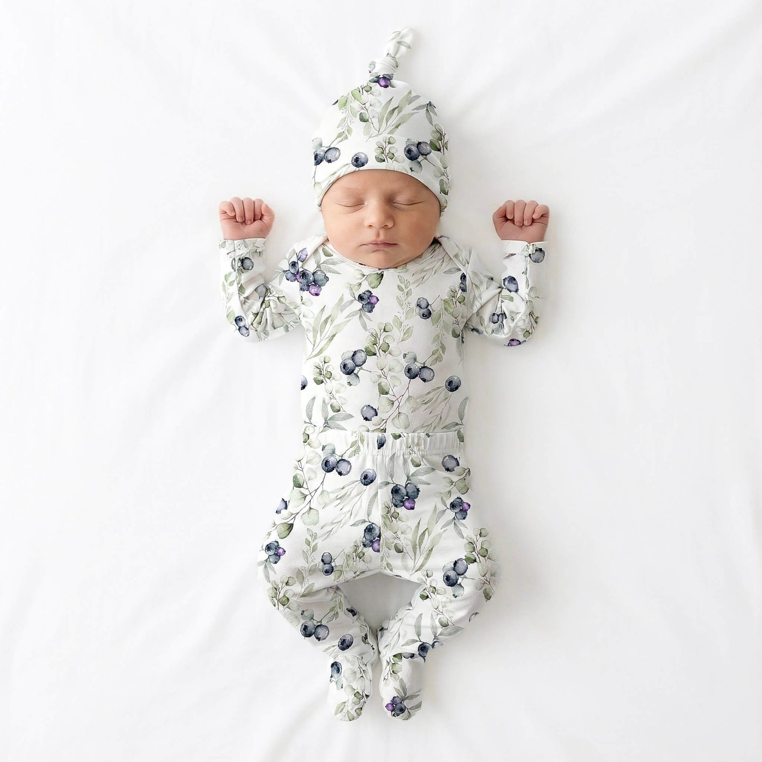 Baby in floral onesie and hat lying on a white background