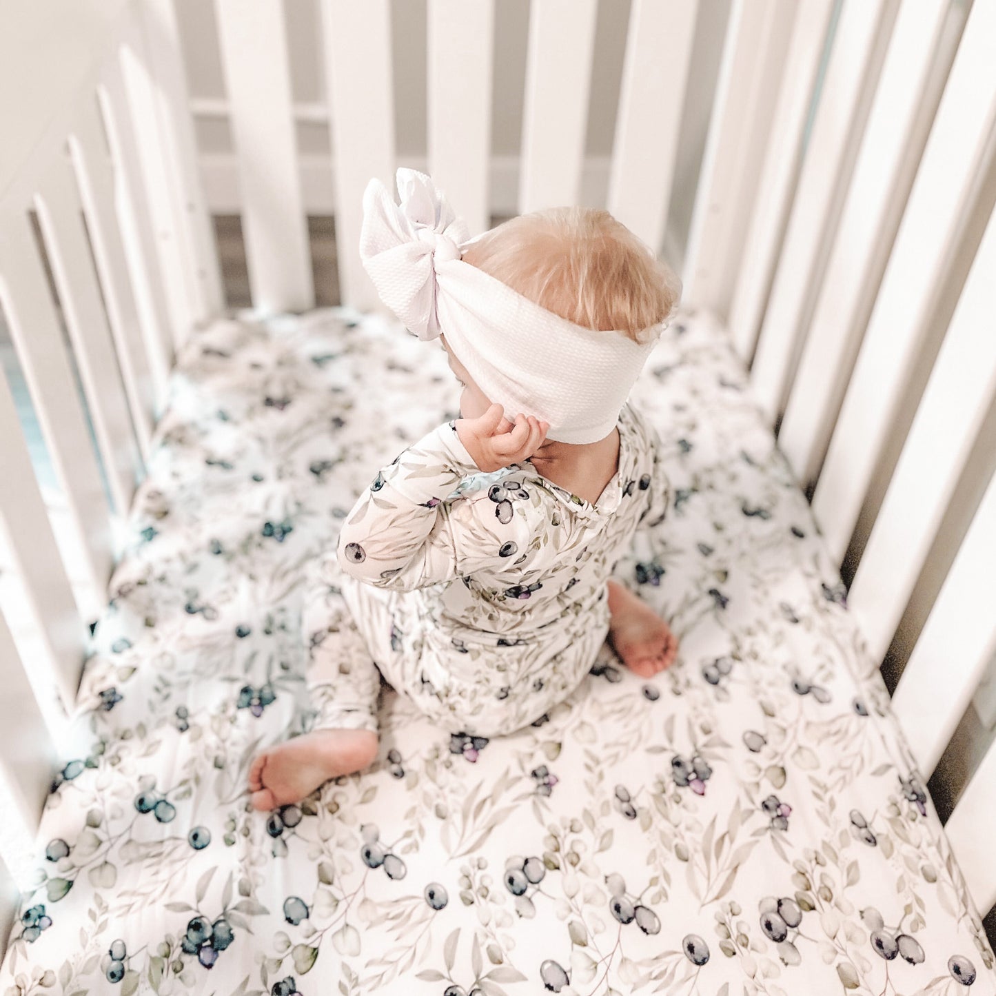 Toddler girl wearing blueberries 2 piece baby pajamas  while sitting on her crib 