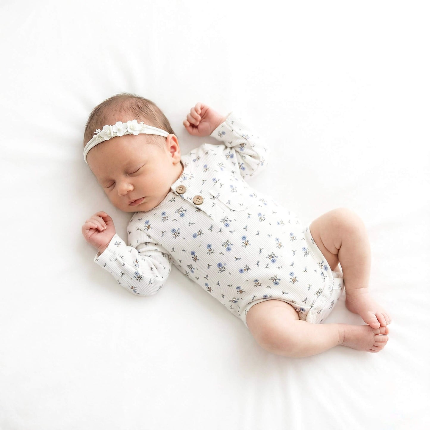 Newborn baby wearing a floral onesie and headband on a white background