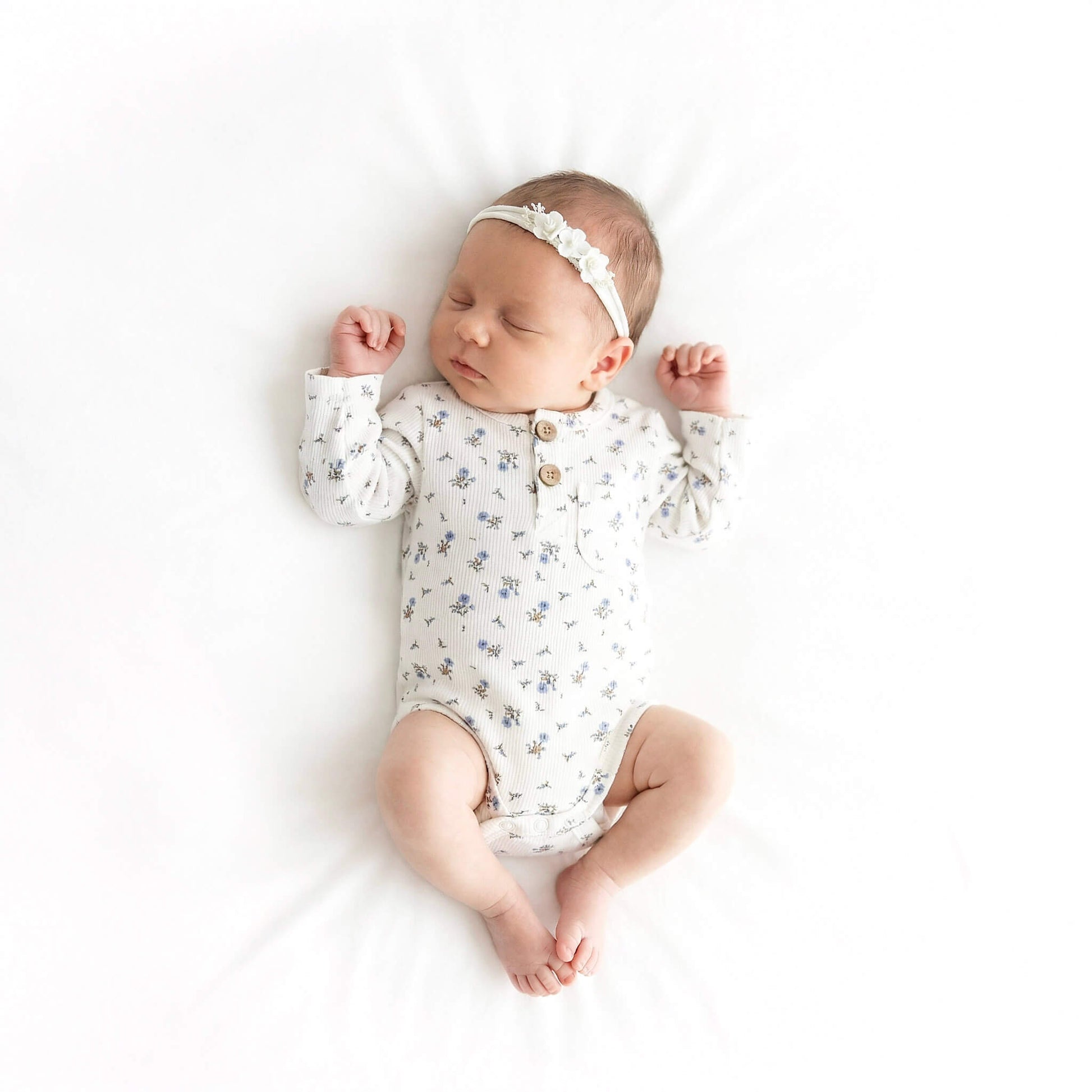 Newborn baby wearing a floral onesie and headband on a white background