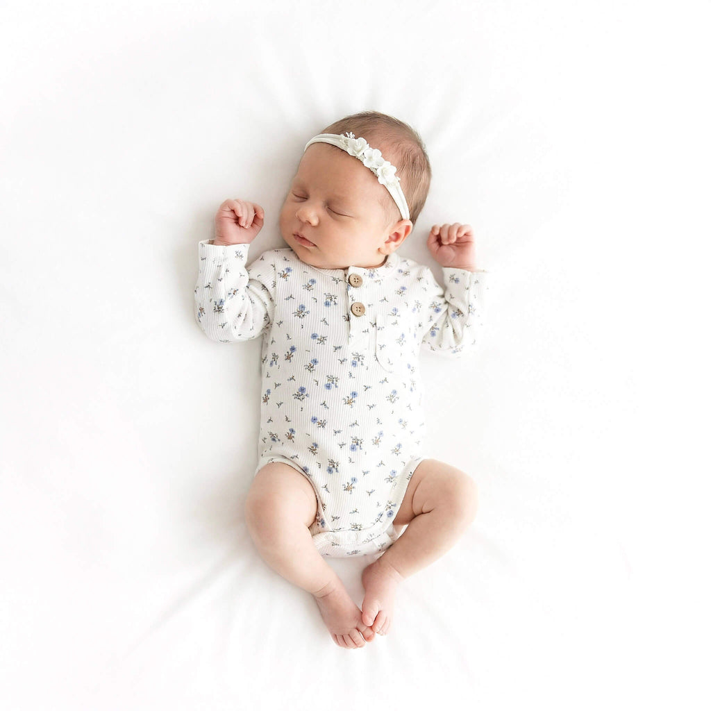 Newborn baby wearing a floral onesie and headband on a white background