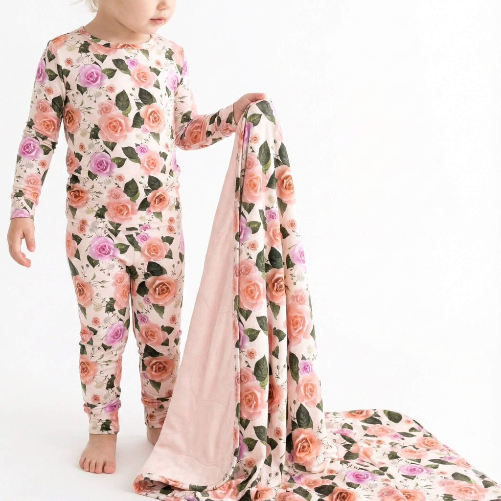 Child wearing a floral onesie holding a matching blanket on a white background