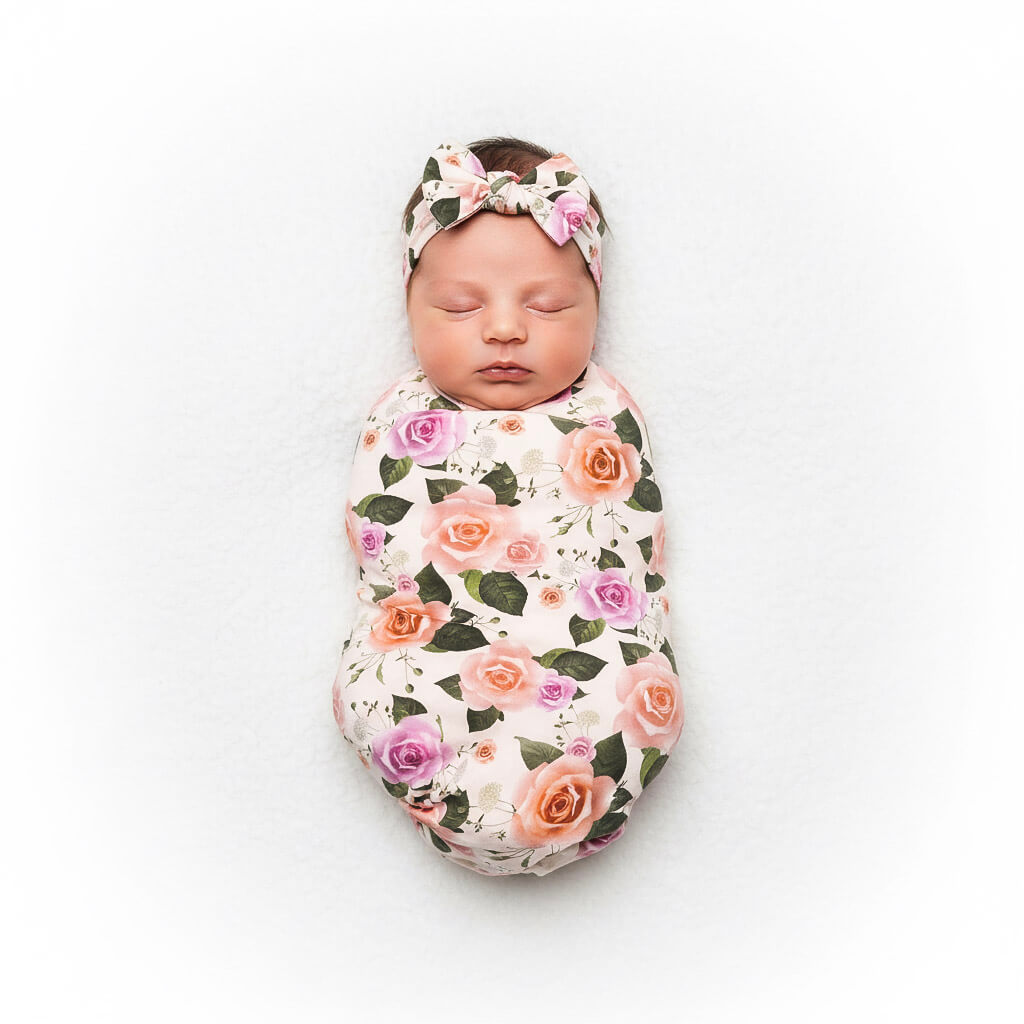 Newborn baby swaddled in a floral blanket with a matching headband on a white background
