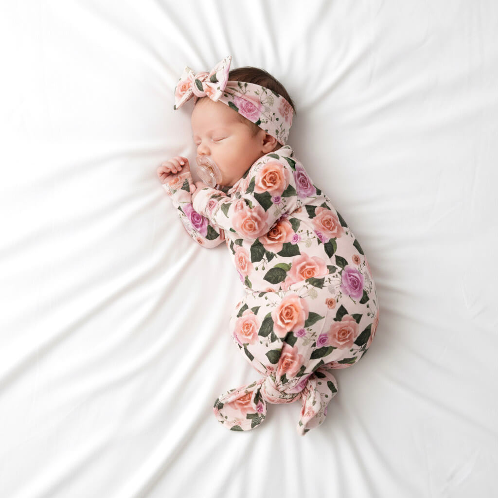 Newborn baby wrapped in a floral swaddle with a matching headband on a white background