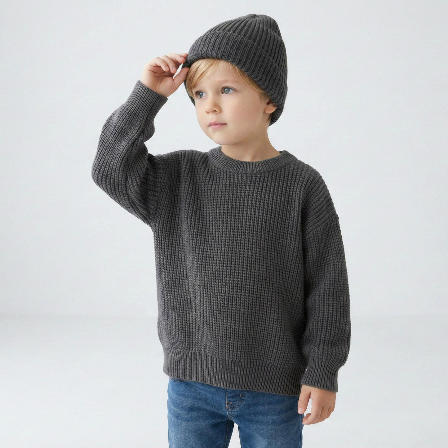 Child wearing a gray sweater and knit hat on a white background