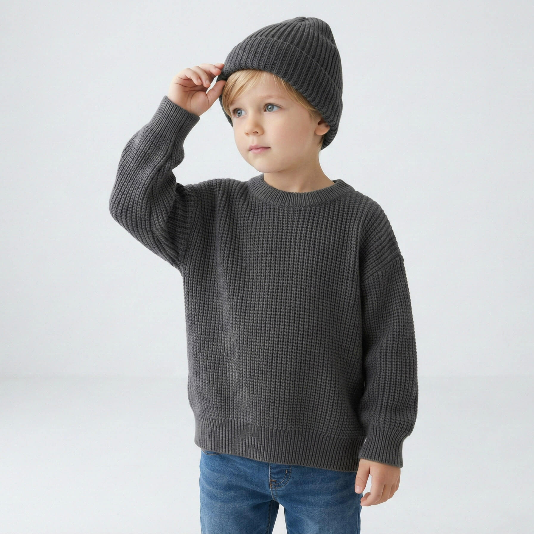 Child wearing a gray sweater and knit hat on a white background