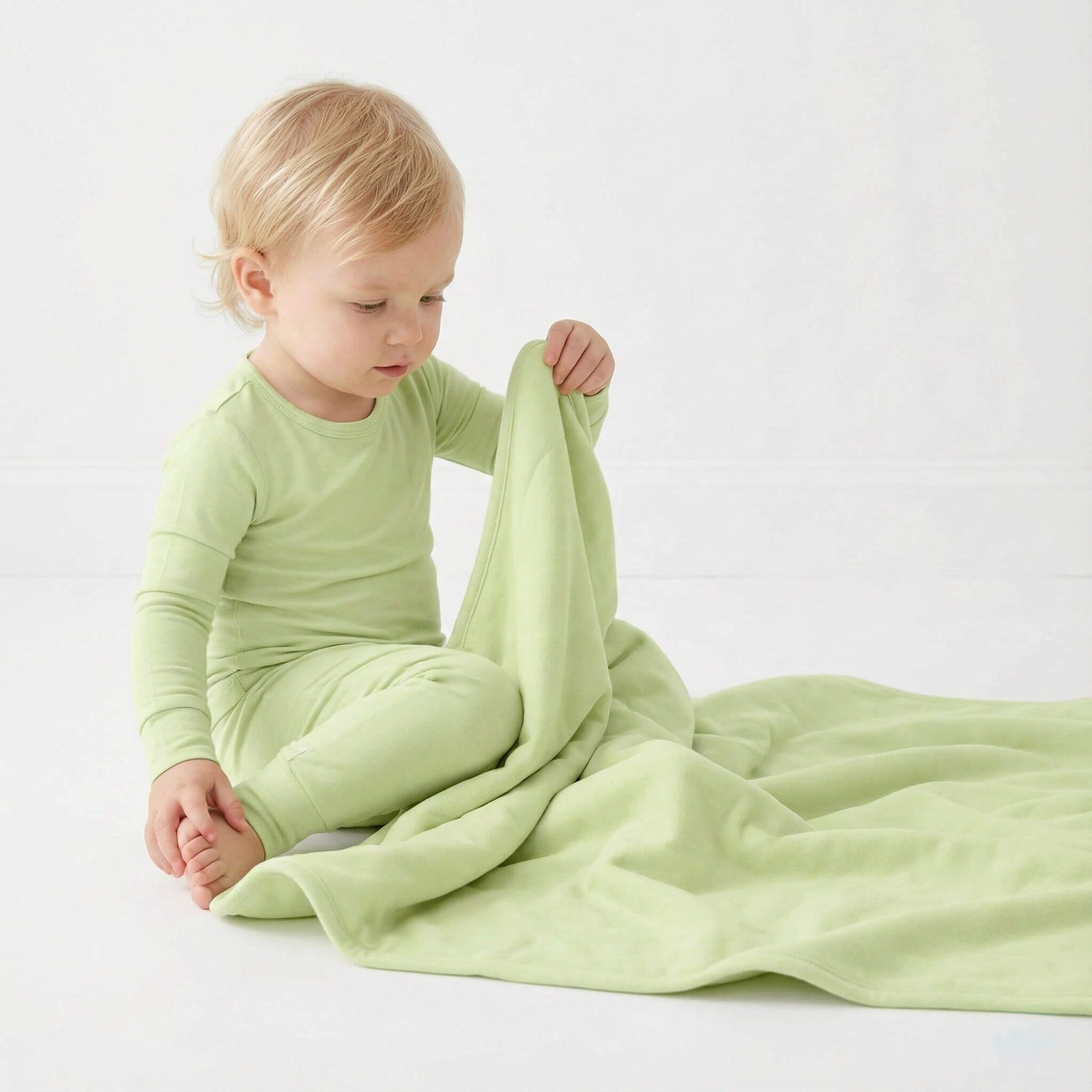 Child in green pajamas holding a green blanket on a white background