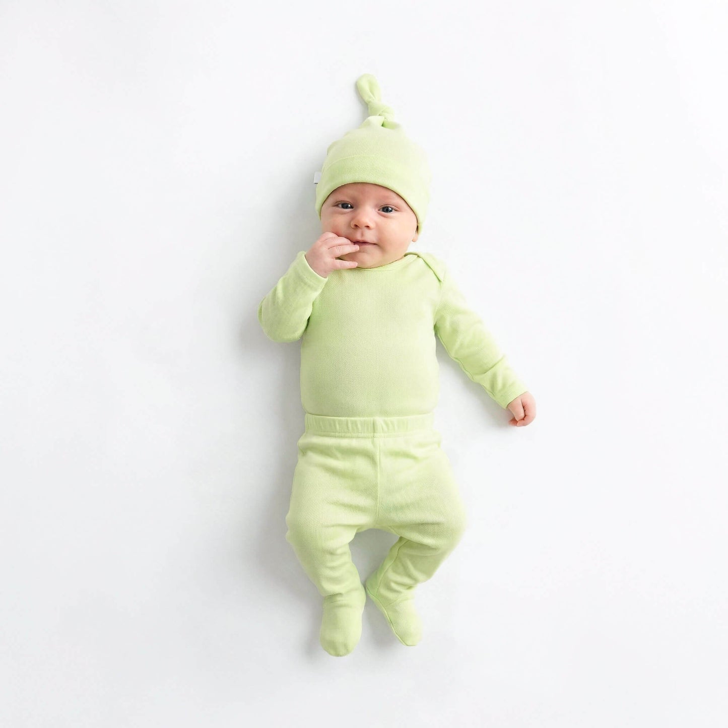 Baby in a light green outfit with a matching hat on a white background