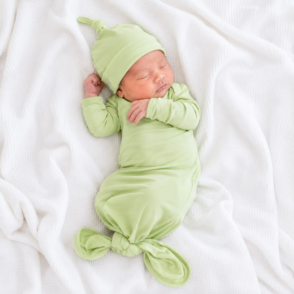 Newborn baby wrapped in a green gown and beanie on a white background