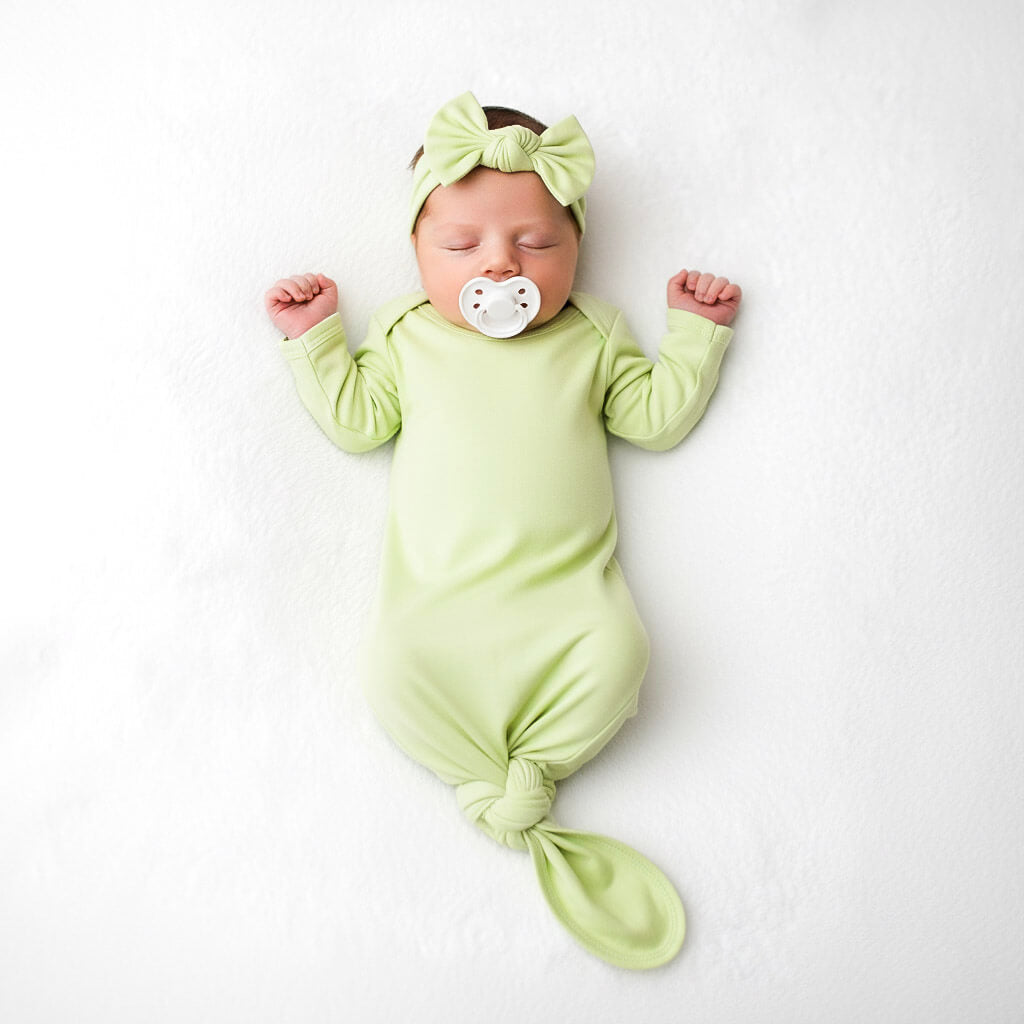 Newborn baby wrapped in a green swaddle and headband with a pacifier on a white background