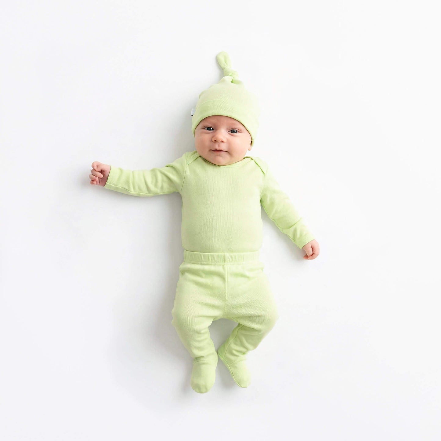 Baby in a green outfit with a matching hat on a white background
