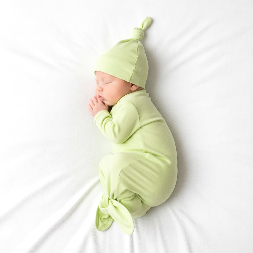 Newborn baby wrapped in a light green swaddle and hat on a white background