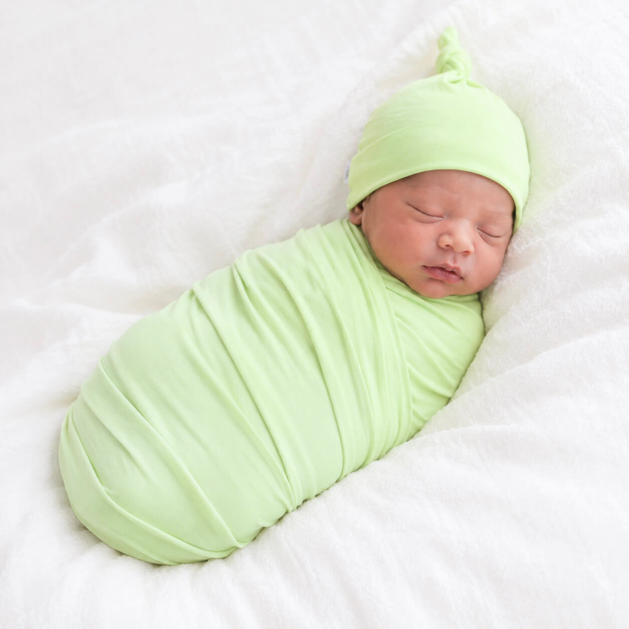 Newborn baby swaddled in a light green blanket and hat on a white background