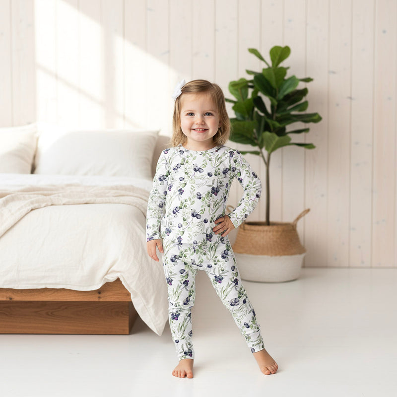 Child wearing a blueberry pajama set in a bright bedroom.