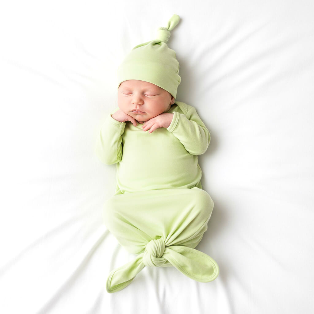 Newborn baby wrapped in a green swaddle and hat on a white background