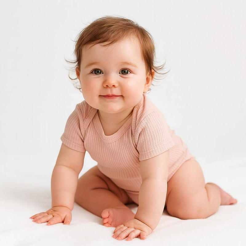 Baby in a pink onesie sitting on a white surface